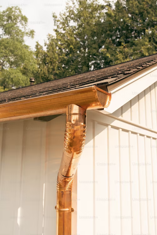 Clean gutters protecting a home from water damage by https://unsplash.com/photos/a-close-up-of-a-gutter-hose-on-the-side-of-a-house-05zj7SMw16Q